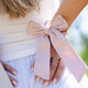 Close-up of a person wearing pale linen clothes with kooshoo's stylish satin bow on her wrist. 