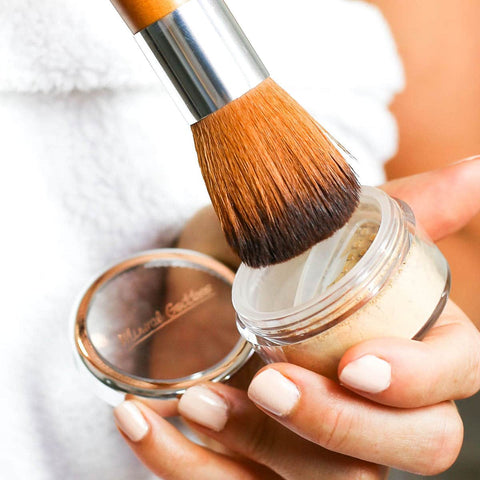 Person holding loose setting powder and dipping Kylie's Professional brush into pot.
