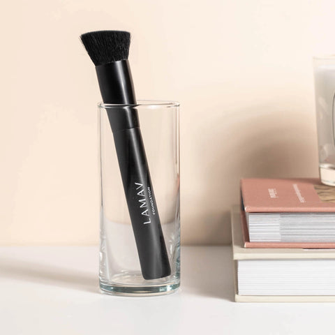LAMAV foundation brush in a glass on a desk with books to the side.