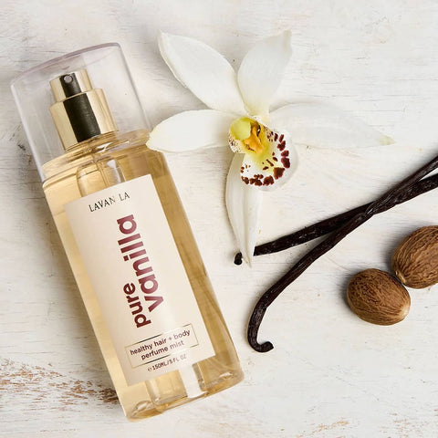 Lavanila Pure Vanilla 150ml perfume mist bottle with vanilla beans and an orchid on a light wooden surface.