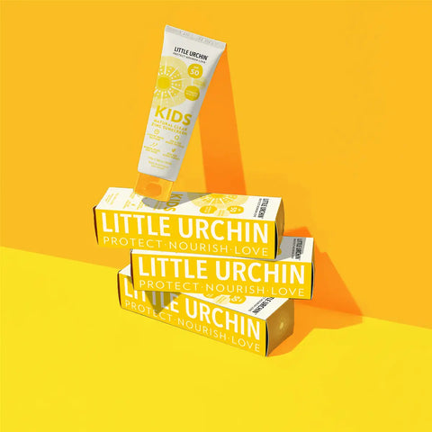 A tube of Little Urchin Kids Sunscreen Lotion and two matching product boxes are arranged in a stylised studio composition on a bright yellow background.