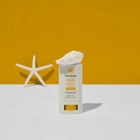 Little Urchin Kids Natural Sunscreen Stick SPF 50+ in a white stick container with a seashell on top, set against a split yellow and white background with a white starfish prop.