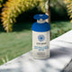 Lifestyle shot of Little Urchin Natural Clear Zinc Sunscreen SPF 50 300g pump bottle on a pale stone ledge in front of a sunny green garden