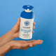 Lifestyle shot of a hand holding the Little Urchin Natural Clear Zinc Sunscreen SPF 50 300g pump bottle against a bright blue background