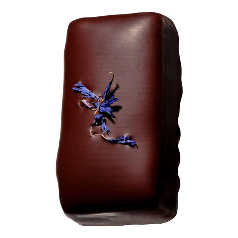 A single dark chocolate bar with a small blue flower decoration on the front, set against a plain white background.