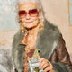 Elderly woman wearing sunglasses and a fur coat, holding an open Luvio peppermint bar with a bite taken out.