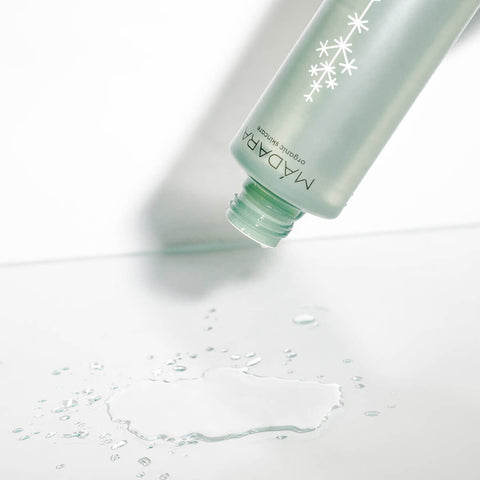 Green bottle releasing water droplets on a light grey background.