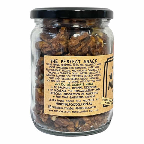A clear glass jar of Mindful Foods Maple Cinnamon Nuts with a black lid and a tan paper label, shown on a plain white background.