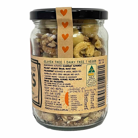 A glass jar of Minigift Foods Almond Husk, showing the back of the label with ingredients, nutrition facts, and a barcode, topped with a black lid decorated with three orange hearts.