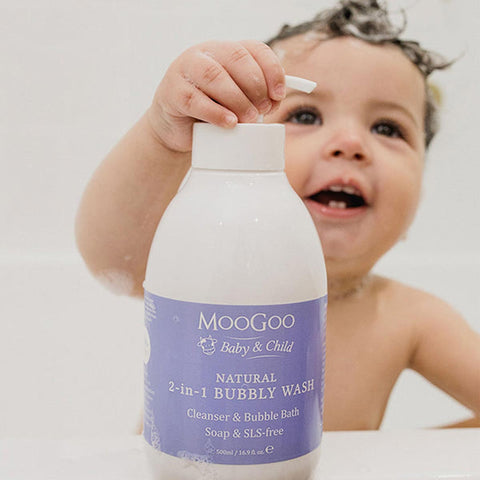 Child holding a bottle of Moogoo Baby & Child Natural Bubbly Wash in a bubble bath