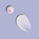 Two drops of white cream on a light purple background.