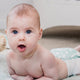 Baby lying on a bed with a neutral background.