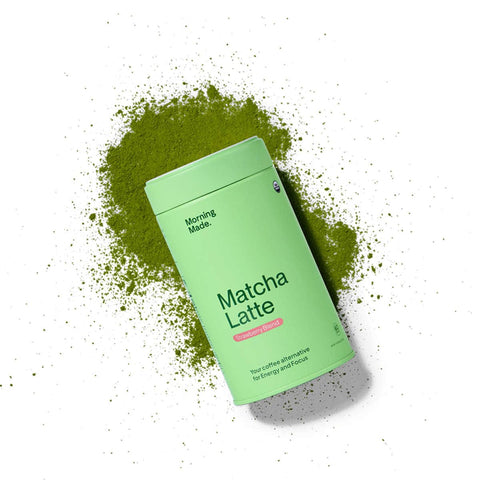 Green container of 'Matcha Latte' powder with matcha powder scattered around on a white background