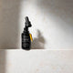 MUKTI Antioxidant Facial Oil on a marbled stone surface with lid off showing dropper filled with oil.