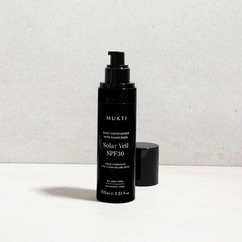Black skincare bottle labelled 'Solar Veil SPF30' by Mukti on a light grey background.