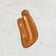 A glossy, metallic bronze-brown cosmetic smear on a textured off-white background.