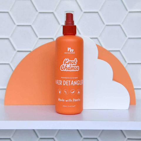Orange hair detangler bottle with brand name on a white & orange geometric background.