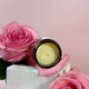 An open round cosmetic jar filled with pale yellow replenish ultra rich moisture cream sits on pink rose petals beside a large pink rose, set against a soft pink background.