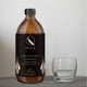 Amber bottle of Qsilica liquid with a black label next to an empty glass on a light grey background.