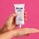 Hand holding a tube of Raww Nourishing Gel Cleanser 100ml against a pink background.