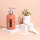 Rose-coloured hand soap dispenser with pump on a white stand against a peach background.