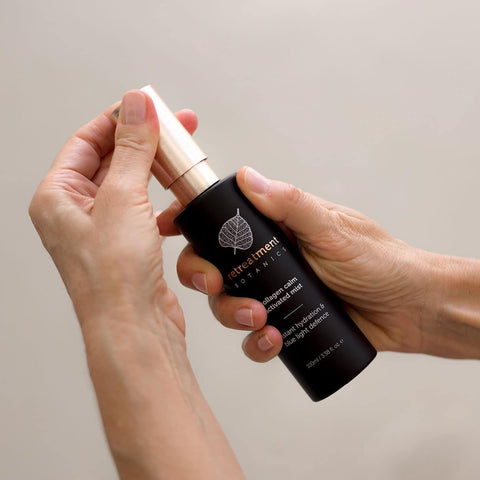 Person holding Retreatment Botanics Collagen Calm Activated Mist 100ml bottle with a dropper against a neutral background.