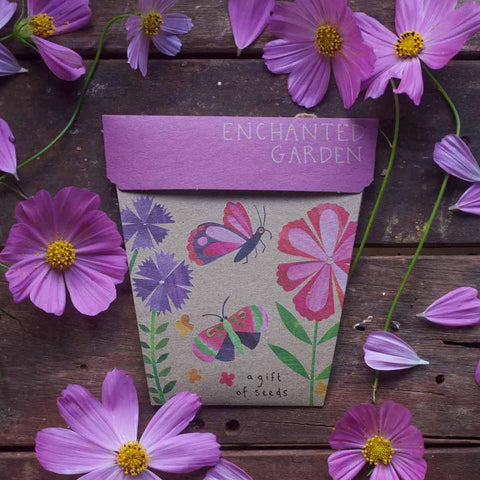 Seed packet with floral design and 'Enchanted Garden' text surrounded by purple flowers on a wooden surface.