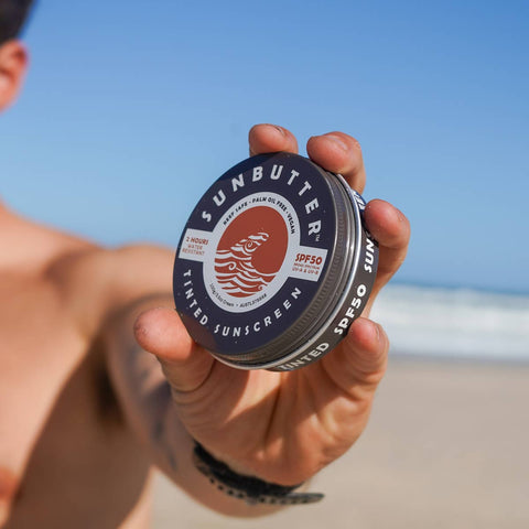 Person holding a SunButter Skincare sunscreen container on a beach.