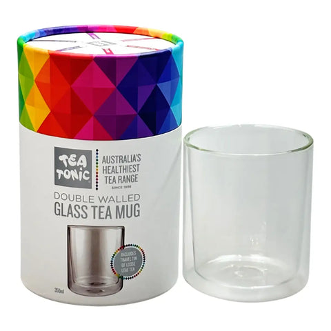 A double-walled clear glass tea mug shown next to its white cylindrical packaging container, which features a colorful geometric pattern on the lid and reads 'Tea Tonic'.