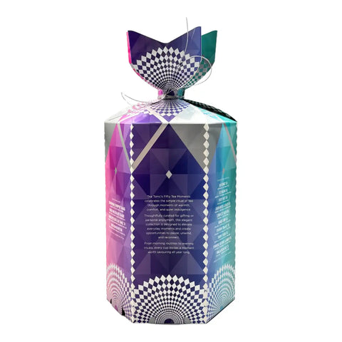 A cylindrical gift box with a colorful geometric pattern in purple, blue, pink, and teal, featuring white text on the front and a decorative paper bow at the top, set against a plain white background.