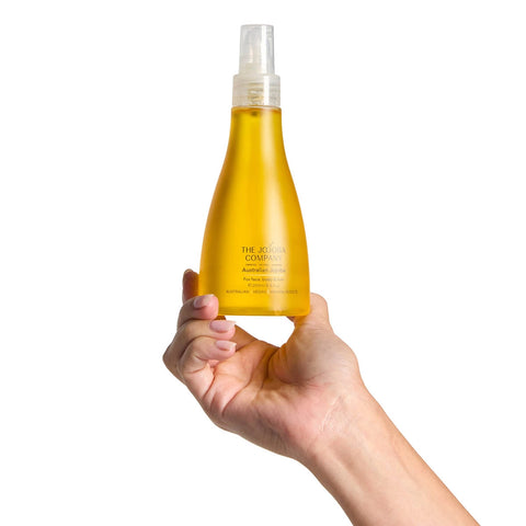 Hand holding a yellow bottle of Australian Jojoba Oil with a white spray nozzle against a white background