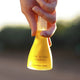 Hand holding a yellow bottle labeled 'The Jojoba Company Australian Jojoba' against a blurred natural background
