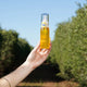 Hand holding a bottle of calming jojoba with a blurred natural background