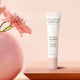 Firming eye balm tube from The Jojoba Company with a pink flower on a peach background.