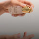 Hand holding a bottle of 'The Jojoba Company' serum with a gold cap, dripping serum onto skin.