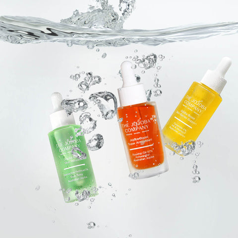 Three bottles of The Jojoba Company skincare products with water droplets and splashes.