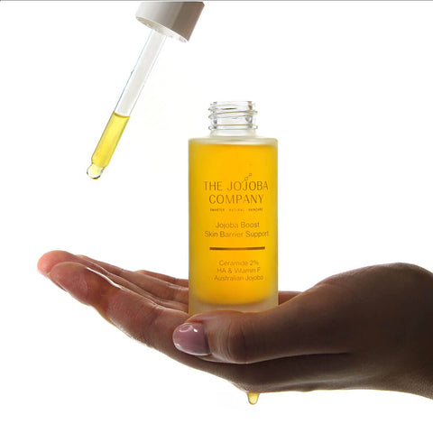Bottle of 'The Jojoba Company Jojoba Boost Skin Barrier Support' skincare product held in a hand with a dropper above.