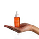 Orange skincare serum bottle with dropper held in a hand on a white background.