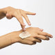 Hand applying ultimate night cream to another hand on a white background