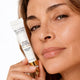 A close-up of a woman holding a white tube of The Jojoba Company Ultimate Plumping Lip Treatment against a clean white background.
