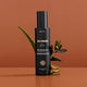 Black bottle of 'Three Warriors' body tan product on an orange background with green leaves.