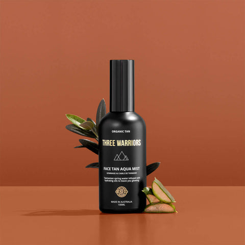 Black bottle of Three Warriors Face Tan Aqua Mist on a brown background.