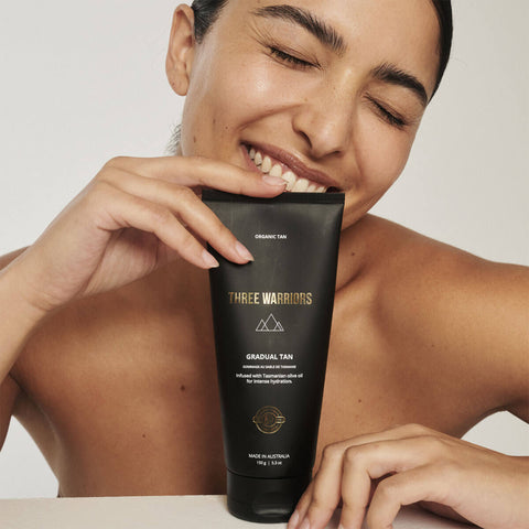 Woman holding a 'Three Warriors gradual tan' product against a neutral background.