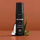 Three Warriors self-tan mousse bottle with aloe vera leaves on a brown background.