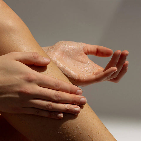 Hand applying a gritty textured cream to another hand against a neutral background.