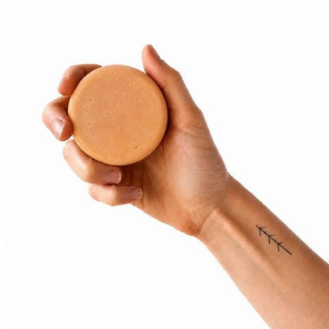 Hand holding a round, orange bar of soap against a white background.