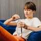 Person holding a water bottle with a brand logo, sitting on a blue couch.