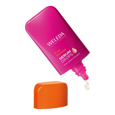 A bottle of Weleda Pore Refining Serum Drops in a vibrant magenta pink color, shown tilted with its bright orange cap resting below.