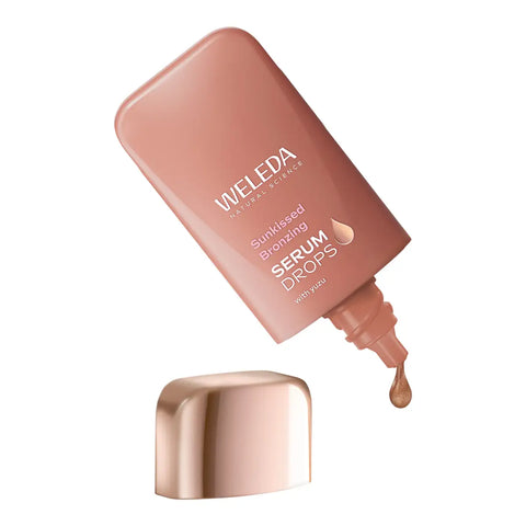 Weleda Sunkissed Bronzing Serum Drops in a metallic rose gold squeeze bottle with its cap removed and a single drop dripping from the tip.