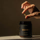 Hand holding a capsule above a Zeally Herbs container on a dark background